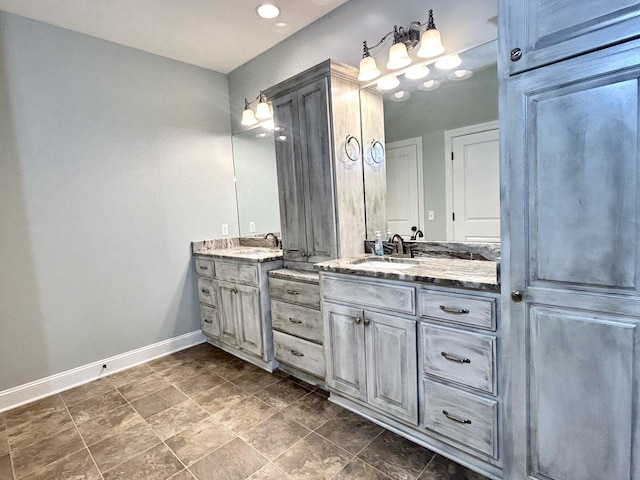 full bathroom featuring baseboards, two vanities, and a sink