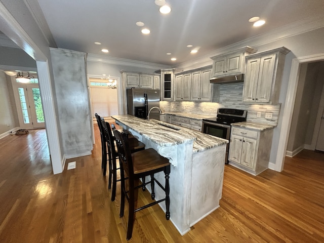 kitchen with stainless steel appliances, decorative backsplash, hardwood / wood-style floors, sink, and a center island with sink