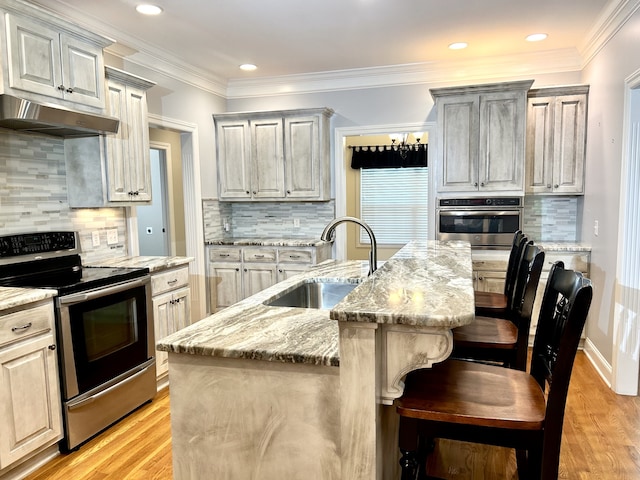 kitchen featuring light wood-type flooring, backsplash, appliances with stainless steel finishes, sink, and a center island with sink