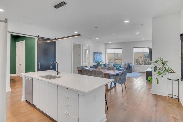 kitchen featuring pendant lighting, a center island with sink, sink, a barn door, and white cabinetry