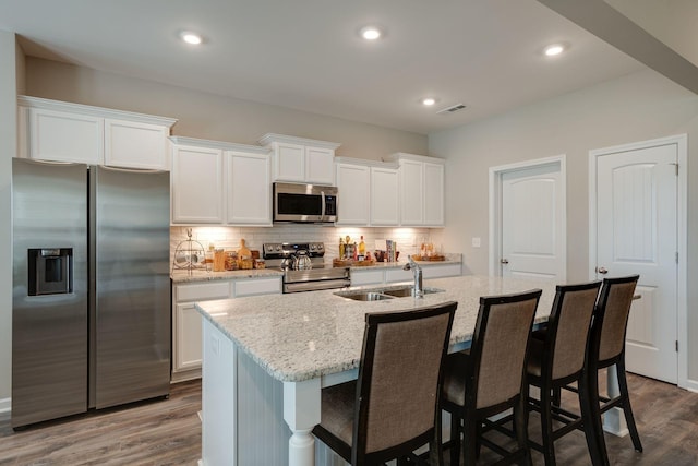 kitchen featuring sink, stainless steel appliances, white cabinets, a center island with sink, and decorative backsplash