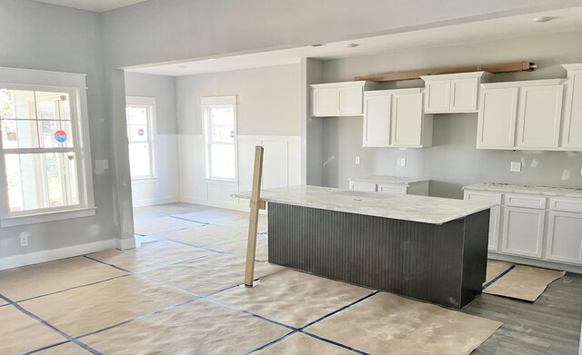 kitchen with light stone counters, a kitchen bar, a center island, and white cabinets