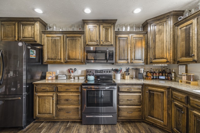 kitchen featuring appliances with stainless steel finishes, a textured ceiling, light stone countertops, and dark hardwood / wood-style floors