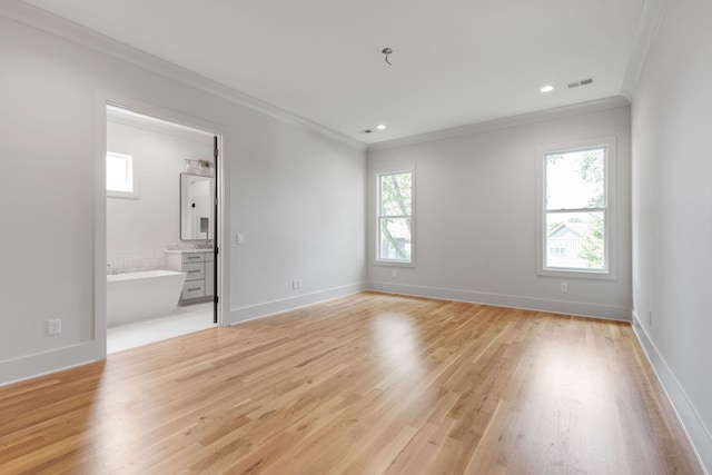 interior space featuring ornamental molding, ensuite bathroom, multiple windows, and light wood-type flooring