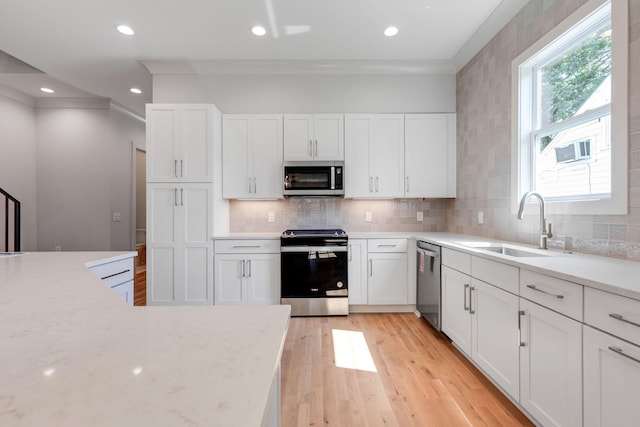 kitchen featuring sink, light hardwood / wood-style flooring, white cabinetry, stainless steel appliances, and light stone counters