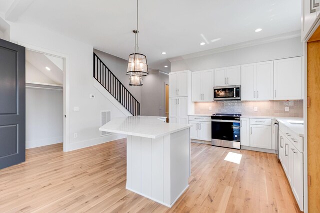 kitchen featuring decorative light fixtures, white cabinets, decorative backsplash, stainless steel appliances, and light hardwood / wood-style flooring