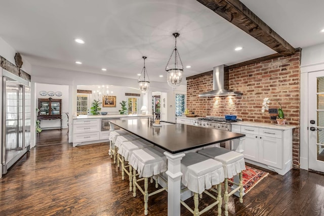 kitchen with wall chimney range hood, dark wood-type flooring, white cabinets, hanging light fixtures, and range