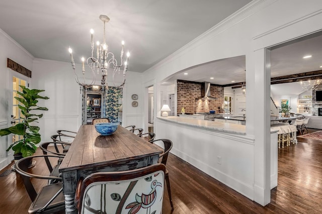 dining space with a notable chandelier, dark wood-type flooring, crown molding, and a stone fireplace