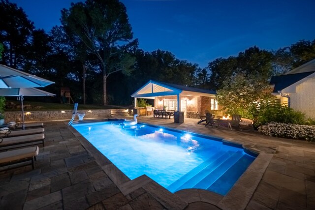 pool at night featuring a patio area and an outdoor structure