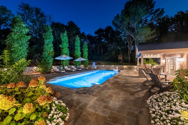 pool at twilight featuring an outdoor structure and a patio area