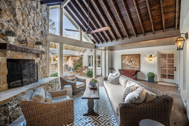 sunroom / solarium with ceiling fan, vaulted ceiling with beams, and an outdoor stone fireplace