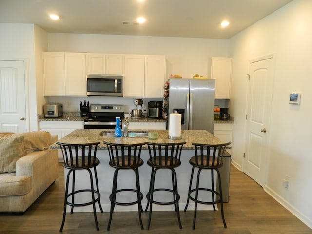 kitchen with a kitchen island with sink, dark wood-type flooring, white cabinetry, appliances with stainless steel finishes, and a kitchen bar