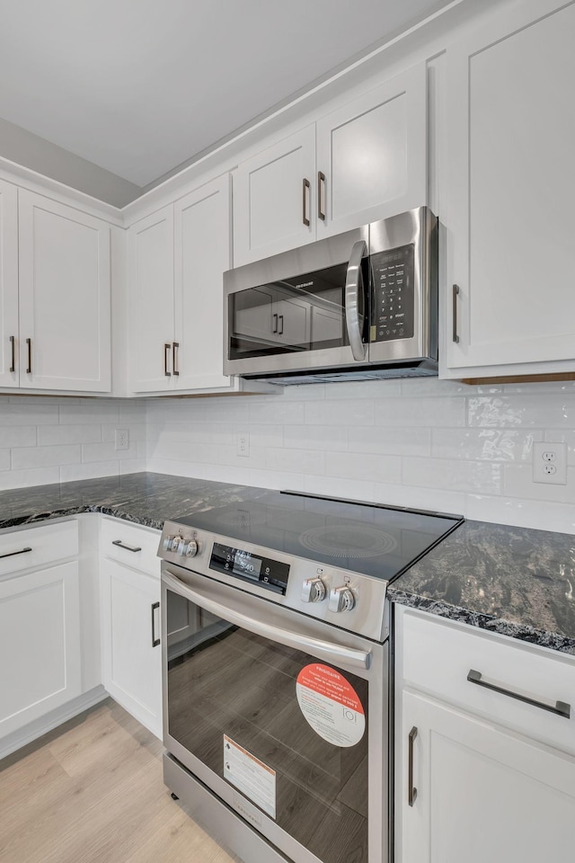 kitchen with appliances with stainless steel finishes, tasteful backsplash, light hardwood / wood-style floors, white cabinets, and dark stone counters