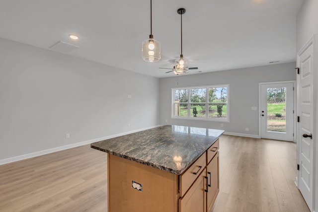 kitchen featuring ceiling fan, dark stone countertops, a center island, light hardwood / wood-style floors, and decorative light fixtures