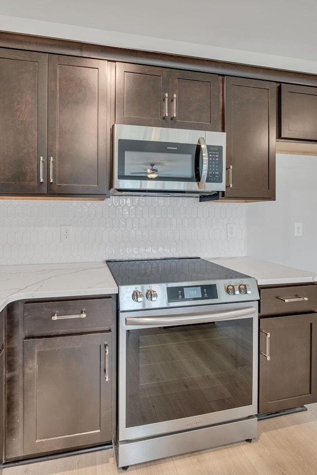 kitchen featuring dark brown cabinets, light stone countertops, light wood-type flooring, and stainless steel appliances