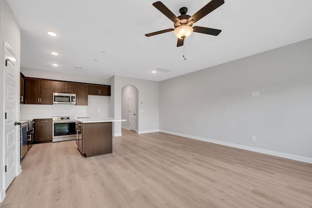 kitchen featuring ceiling fan, stainless steel appliances, backsplash, light hardwood / wood-style floors, and a kitchen island