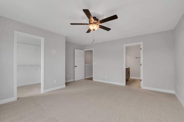 unfurnished bedroom featuring light carpet, ensuite bathroom, a walk in closet, ceiling fan, and a closet