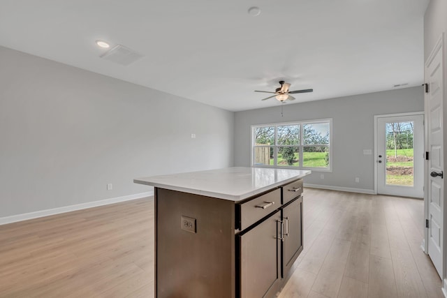 kitchen with light stone countertops, light wood-type flooring, dark brown cabinetry, ceiling fan, and a center island