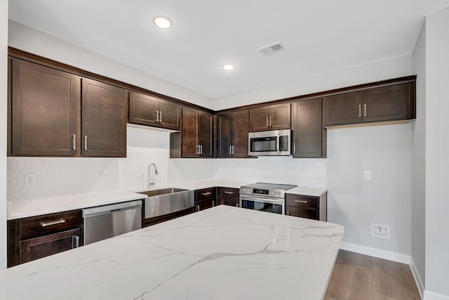 kitchen with sink, light stone countertops, appliances with stainless steel finishes, tasteful backsplash, and dark brown cabinets