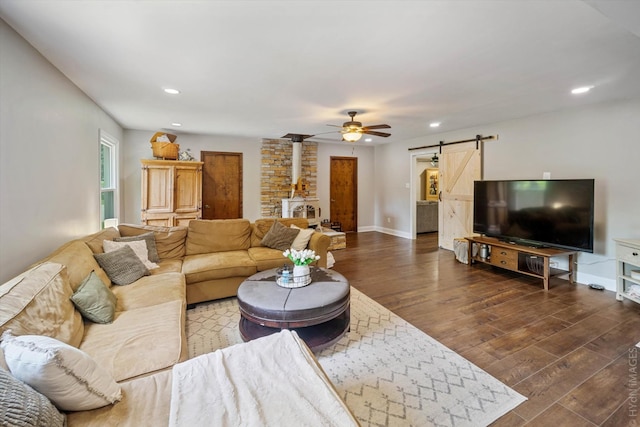 living room with ceiling fan, a barn door, dark hardwood / wood-style flooring, and a wood stove