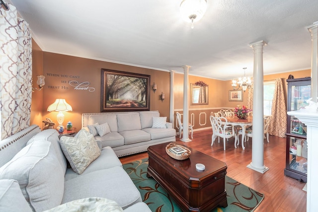 living room featuring decorative columns, wood-type flooring, ornamental molding, and a notable chandelier