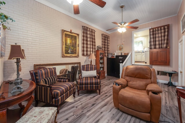 living area featuring ceiling fan, brick wall, ornamental molding, and light hardwood / wood-style floors