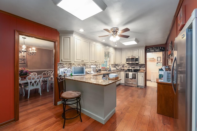 kitchen with white cabinetry, a breakfast bar area, stainless steel appliances, ceiling fan with notable chandelier, and light hardwood / wood-style flooring