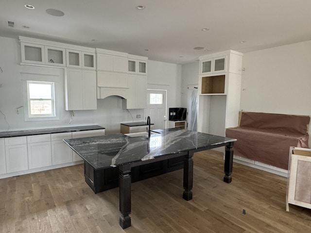 kitchen featuring white cabinetry, dark stone countertops, wood-type flooring, and backsplash