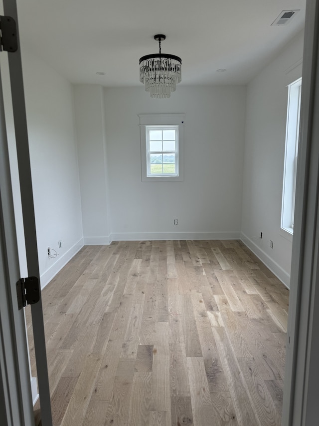 unfurnished room featuring a chandelier and light wood-type flooring