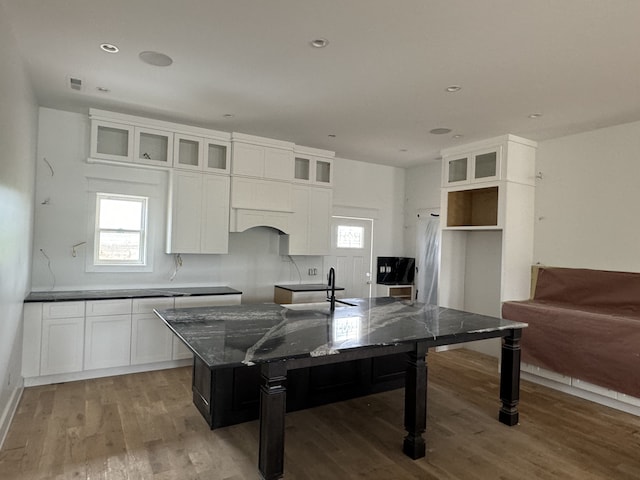 kitchen featuring white cabinetry, wood-type flooring, tasteful backsplash, dark stone countertops, and a kitchen island