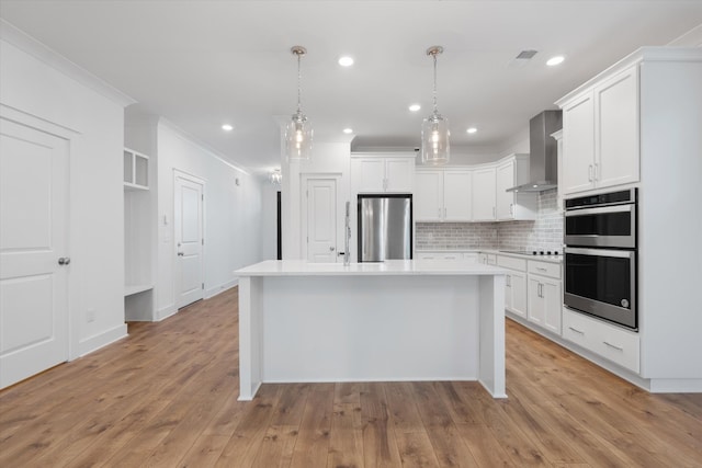 kitchen featuring white cabinetry, decorative light fixtures, a kitchen island, stainless steel appliances, and wall chimney range hood