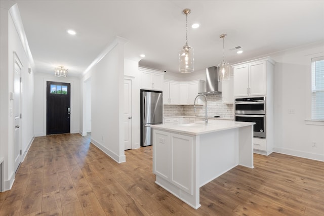 kitchen featuring stainless steel appliances, a kitchen island with sink, white cabinets, and wall chimney exhaust hood