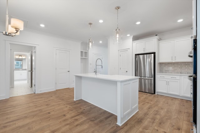 kitchen featuring pendant lighting, stainless steel refrigerator, white cabinetry, backsplash, and a center island with sink