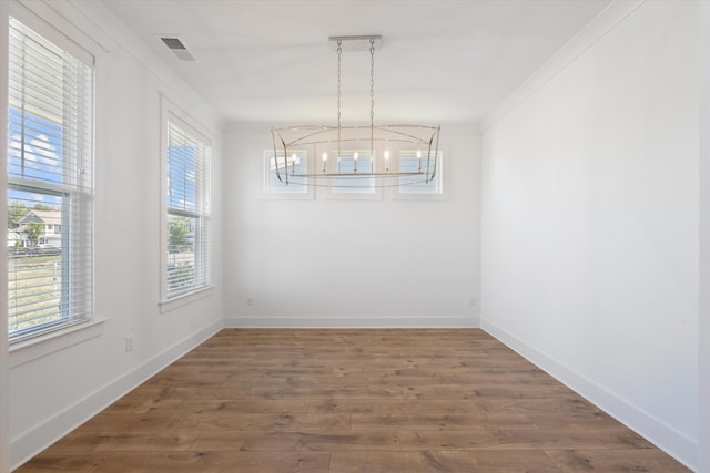 unfurnished dining area featuring a notable chandelier, ornamental molding, dark hardwood / wood-style floors, and a wealth of natural light