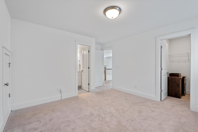 unfurnished bedroom featuring light carpet, ensuite bath, a closet, and a spacious closet