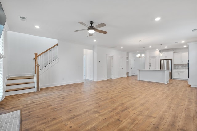 unfurnished living room with crown molding, ceiling fan with notable chandelier, and light hardwood / wood-style flooring