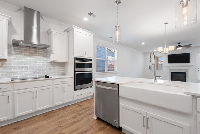 kitchen featuring wall chimney exhaust hood, white cabinetry, decorative light fixtures, appliances with stainless steel finishes, and decorative backsplash