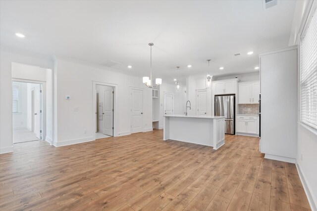 kitchen with tasteful backsplash, decorative light fixtures, stainless steel refrigerator, an island with sink, and white cabinets