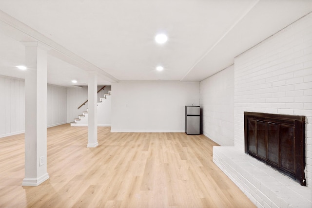 basement with a brick fireplace, stainless steel refrigerator, and light hardwood / wood-style floors