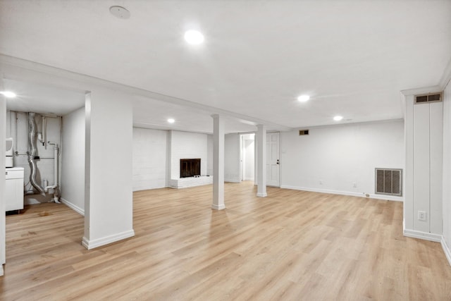 basement with light wood-type flooring, crown molding, and a fireplace