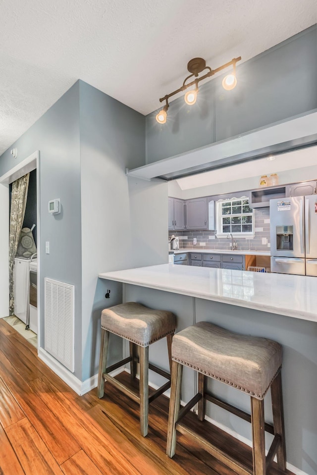 kitchen with tasteful backsplash, stainless steel fridge with ice dispenser, kitchen peninsula, and a kitchen bar