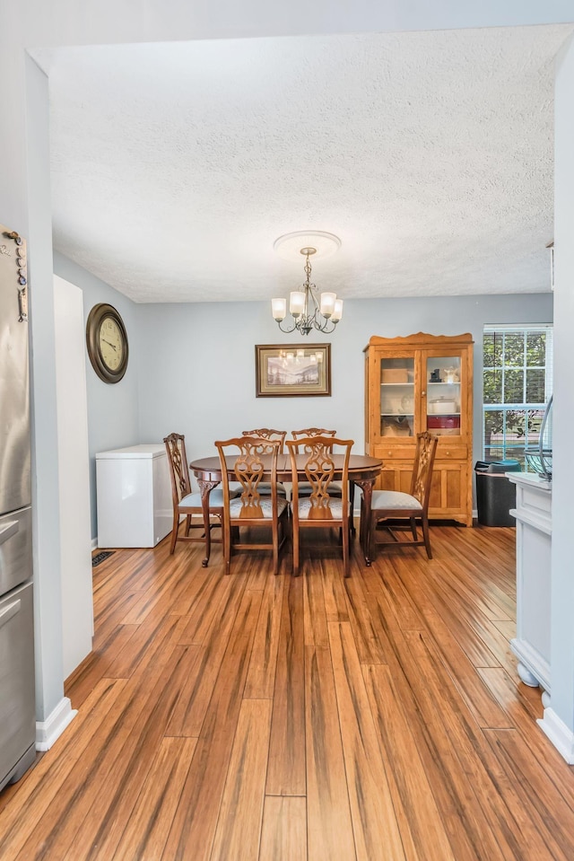 dining space featuring a notable chandelier, light hardwood / wood-style flooring, and a textured ceiling