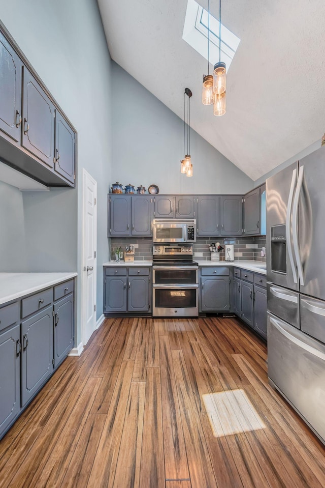 kitchen with tasteful backsplash, a skylight, dark hardwood / wood-style flooring, pendant lighting, and stainless steel appliances