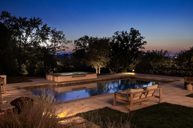 pool at dusk featuring a patio area and an in ground hot tub