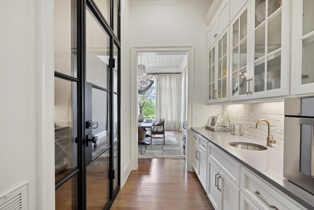 bar with sink, white cabinets, decorative backsplash, light stone countertops, and dark wood-type flooring