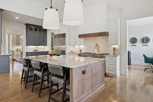 kitchen featuring hanging light fixtures, a kitchen island, stainless steel built in fridge, and white cabinets