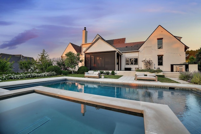 pool at dusk with a patio area and a sunroom