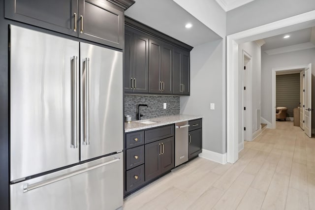 kitchen featuring sink, light stone counters, crown molding, appliances with stainless steel finishes, and decorative backsplash