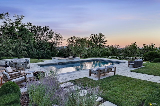 pool at dusk featuring a patio, a lawn, and a jacuzzi