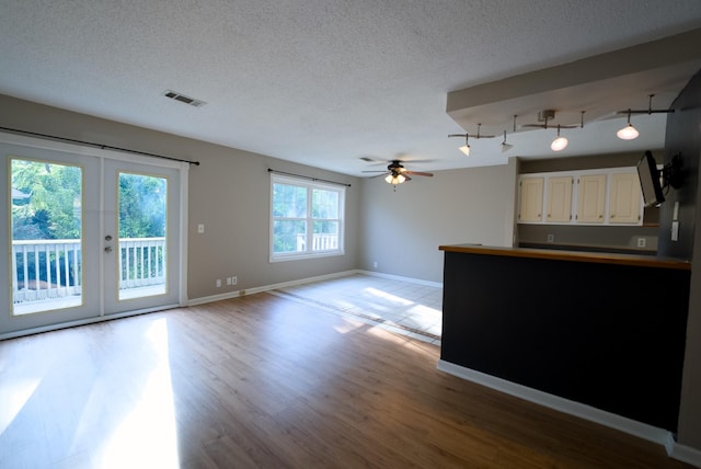 unfurnished living room featuring french doors, ceiling fan, light hardwood / wood-style flooring, and a textured ceiling